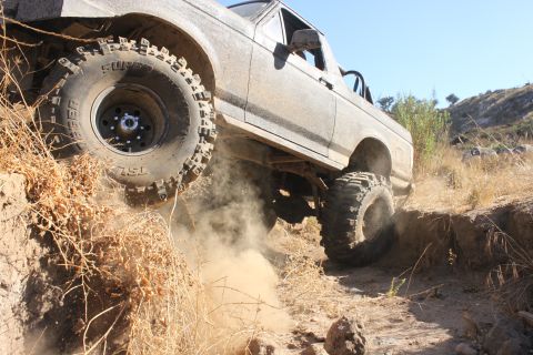 1992 Ford Bronco - This truck is navigating a challenging off-road trail with steep inclines and loose dirt.