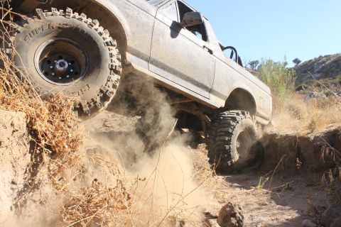 1992 Ford Bronco - A 1992 Ford Bronco navigates a challenging off-road trail, its tires kicking up dust as it ascends a steep incline.