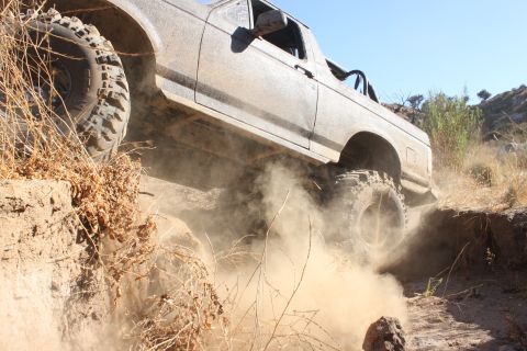 1992 Ford Bronco - A vehicle navigates a challenging off-road terrain, kicking up a cloud of dust.