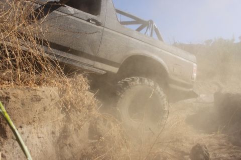 1992 Ford Bronco - A 1992 Ford Bronco navigates a challenging off-road trail, raising a cloud of dust.