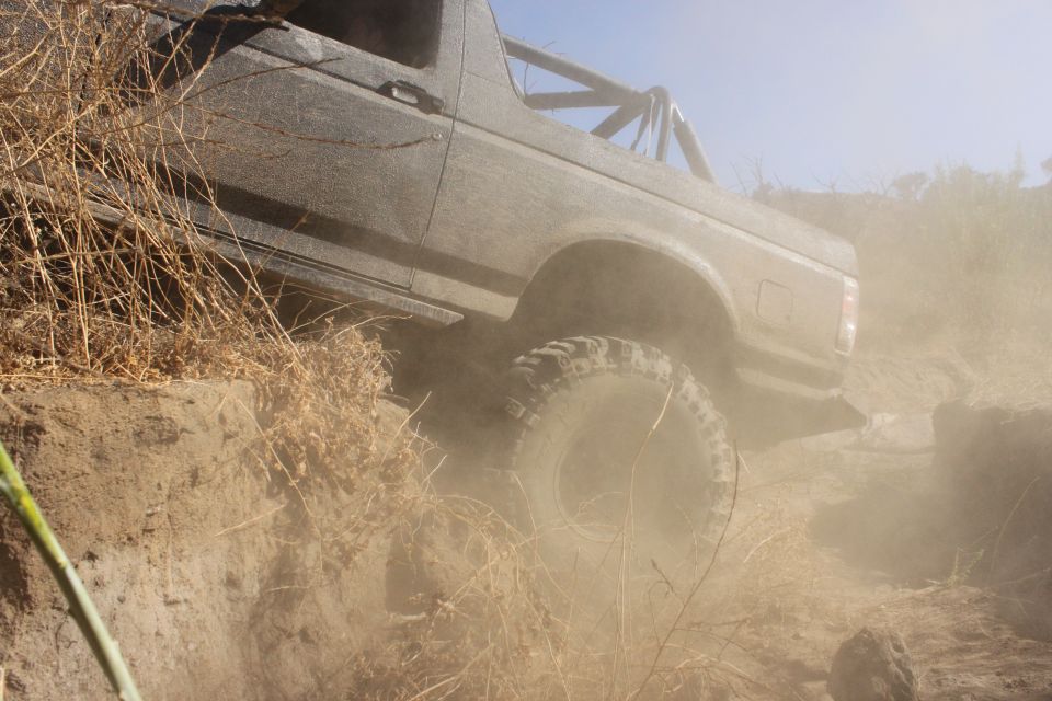 Ford Bronco climbing a dirt embankment, kicking up dust. Roll cage visible