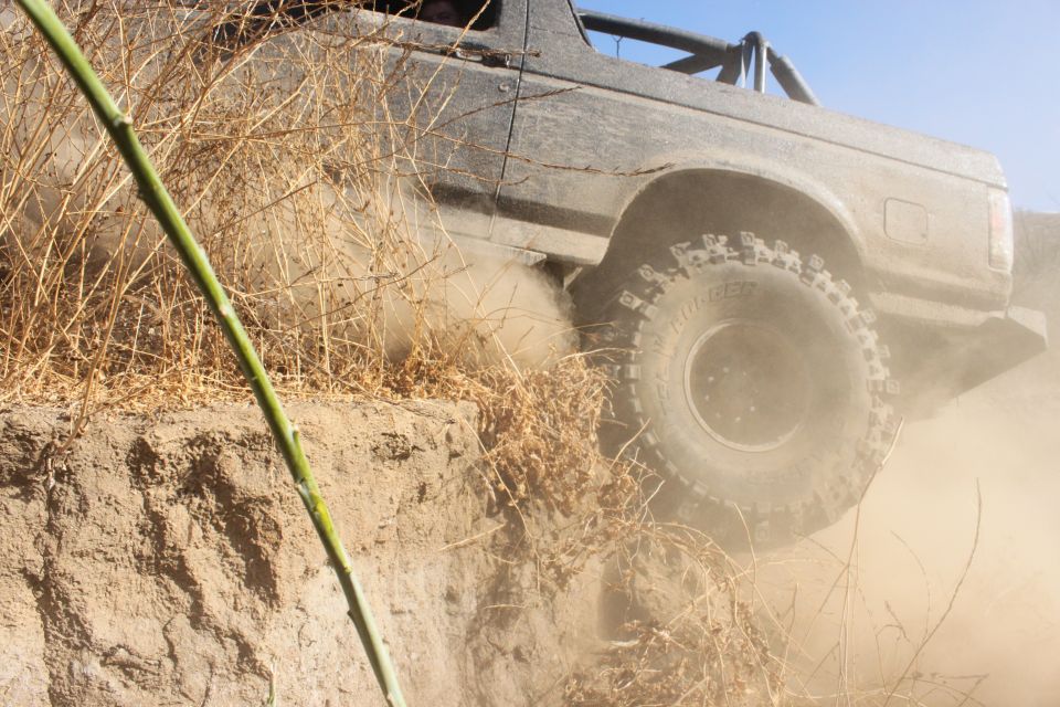 Off-road vehicle kicking up dust as it climbs a steep dirt bank