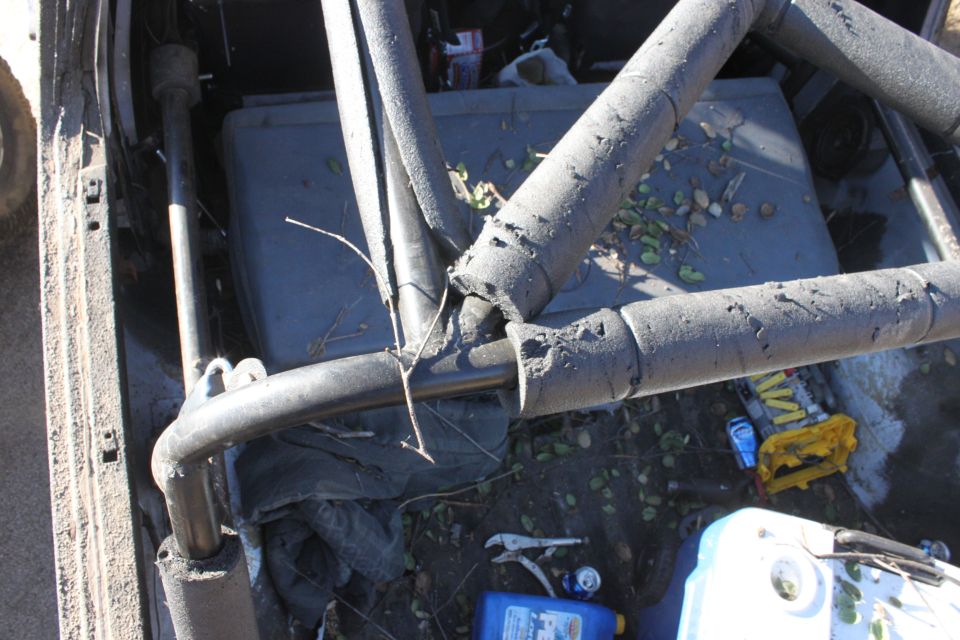 Interior view of a vehicle with a roll cage, debris on the floor, and a yellow tool case