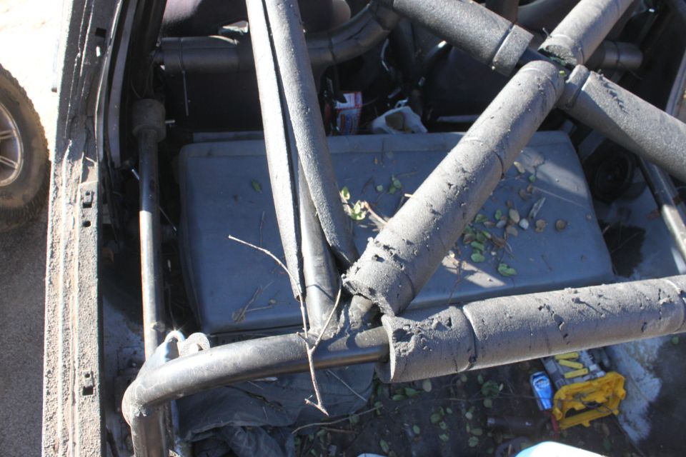 interior view of a vehicle with a roll cage, showing a gray storage bin and debris on the floor