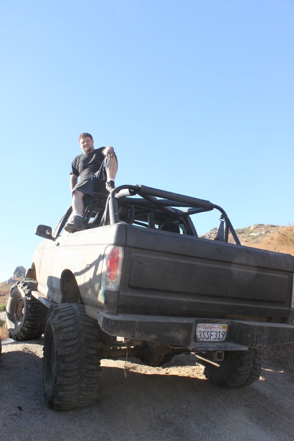 Rear view of a lifted 1992 Ford Bronco with a man sitting on the roof