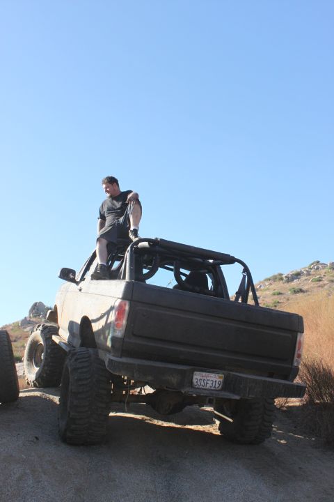 1992 Ford Bronco with large tires and roll cage, man sitting on top. License plate 3SSF319