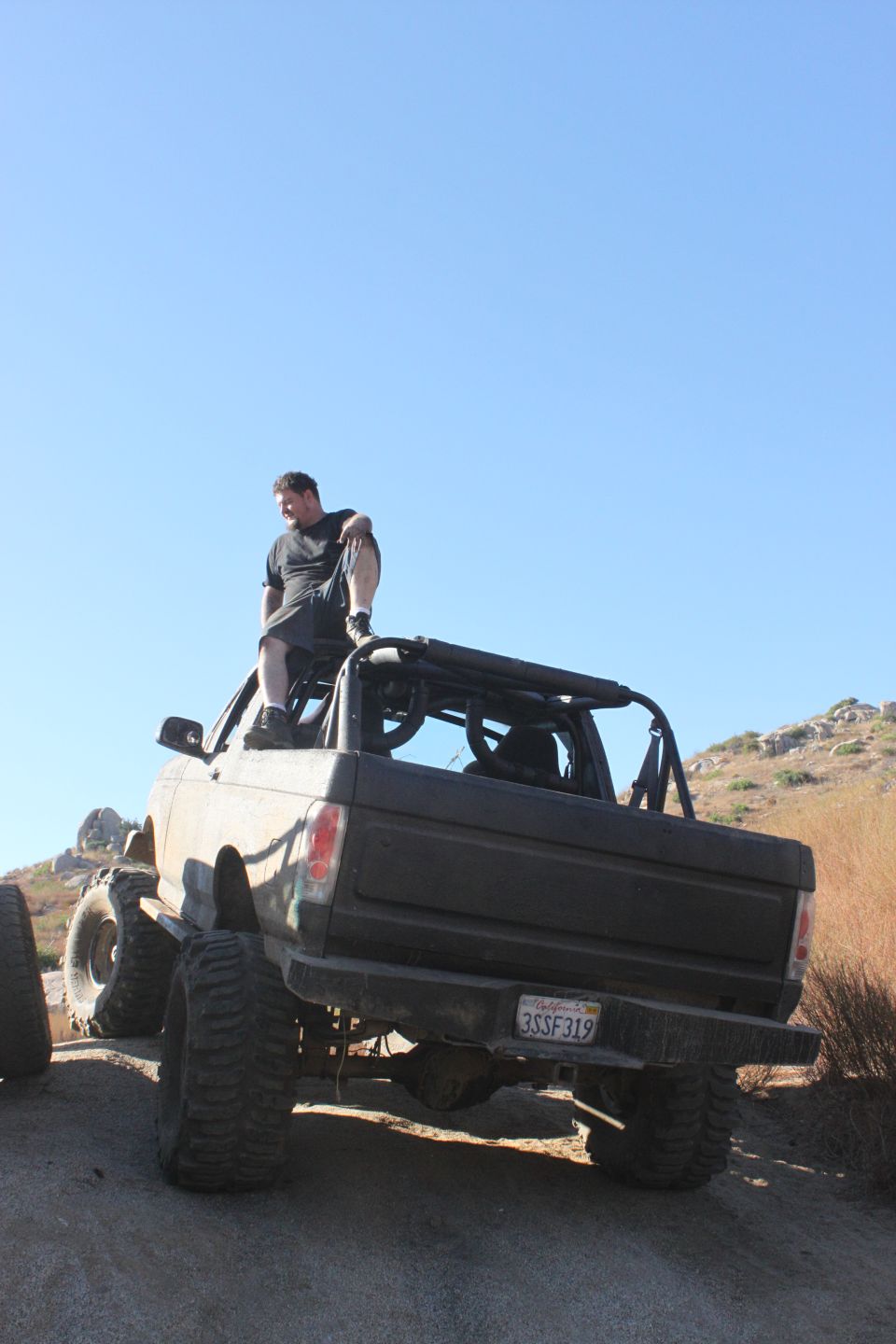 1992 Ford Bronco with large tires and roll cage, man sitting on top. License plate 3SSF319