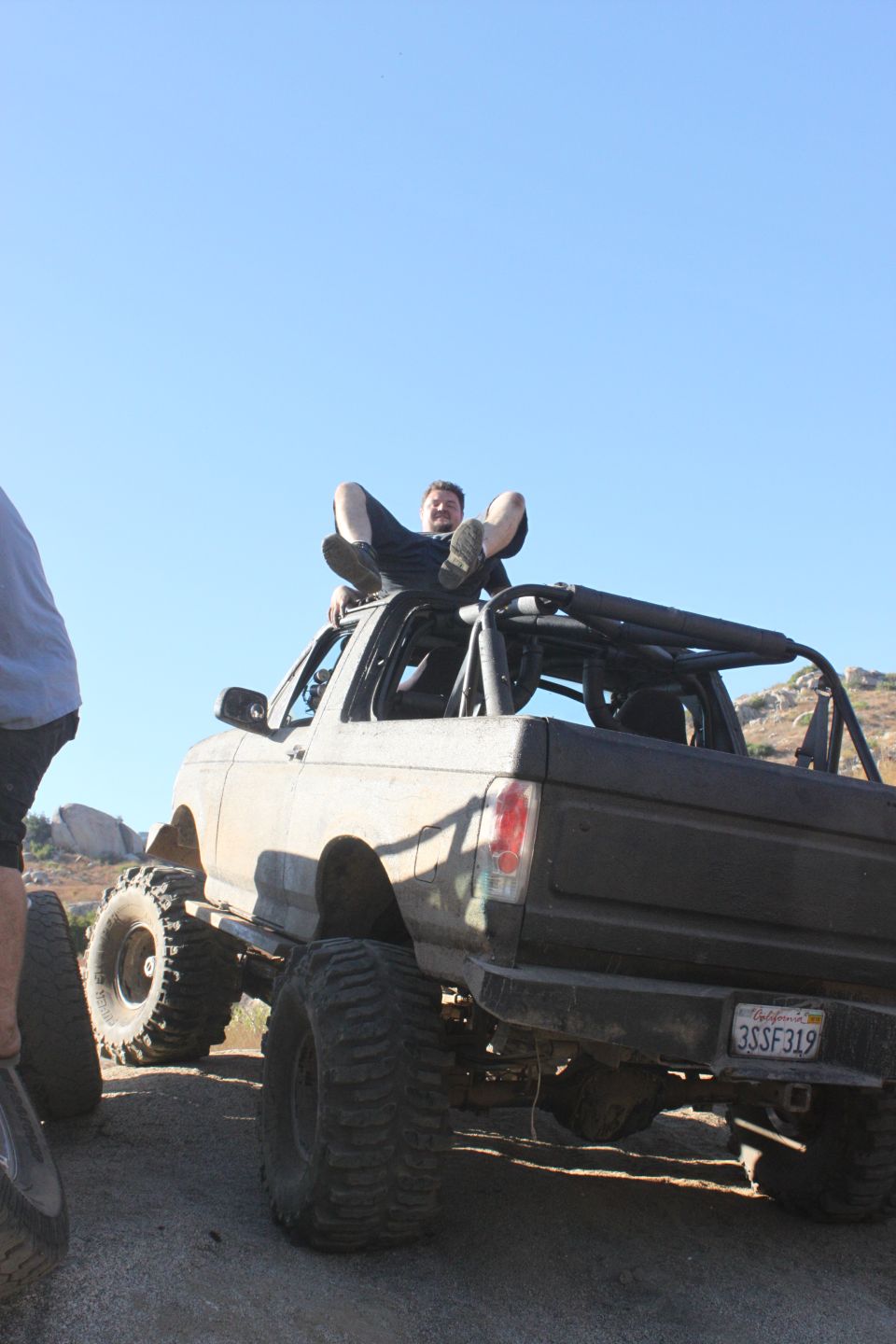 1992 Ford Bronco lifted with large tires, person sitting on roof, California license plate 3SSF319