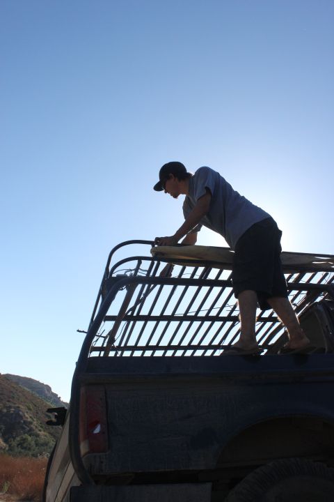 Man on roof rack of dark truck, clear blue sky