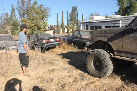 guy standing in a junkyard looking at a black sedan, a black pickup truck, and a lifted black SUV