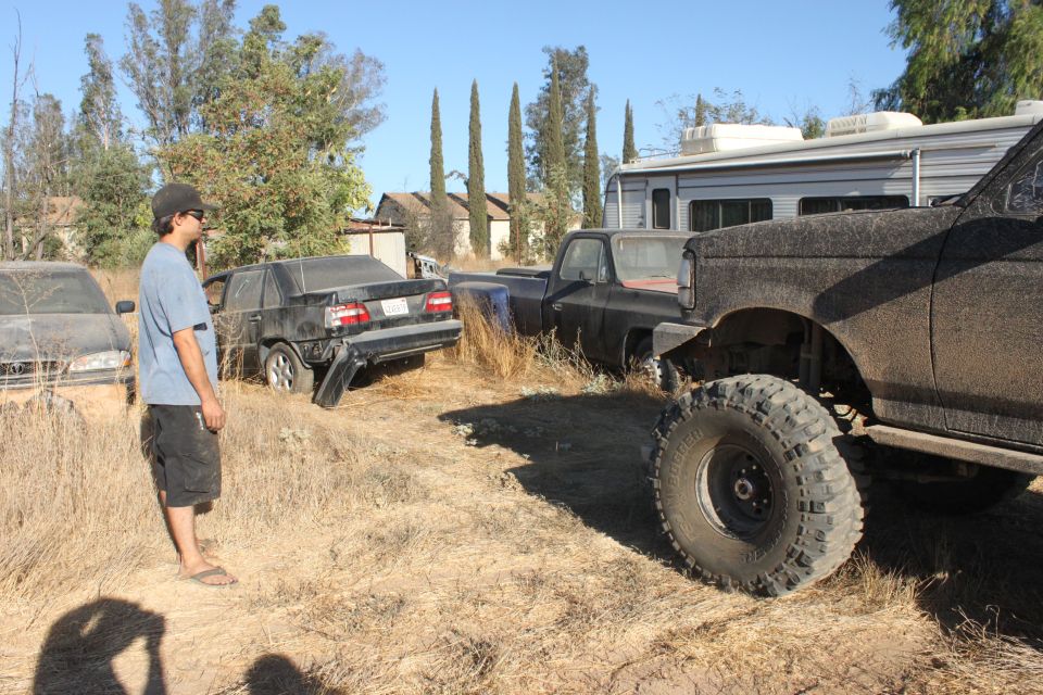 guy standing in a junkyard looking at a black sedan, a black pickup truck, and a lifted black SUV