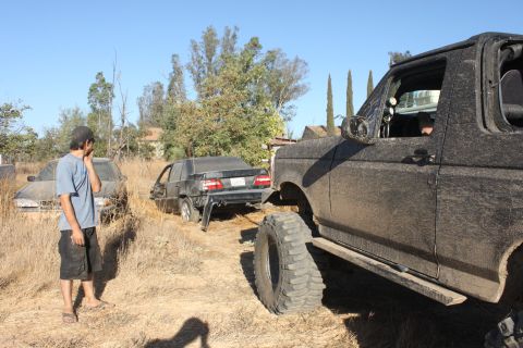Mud-covered 1992 Ford Bronco, 3/4 front view, with a damaged black car behind it