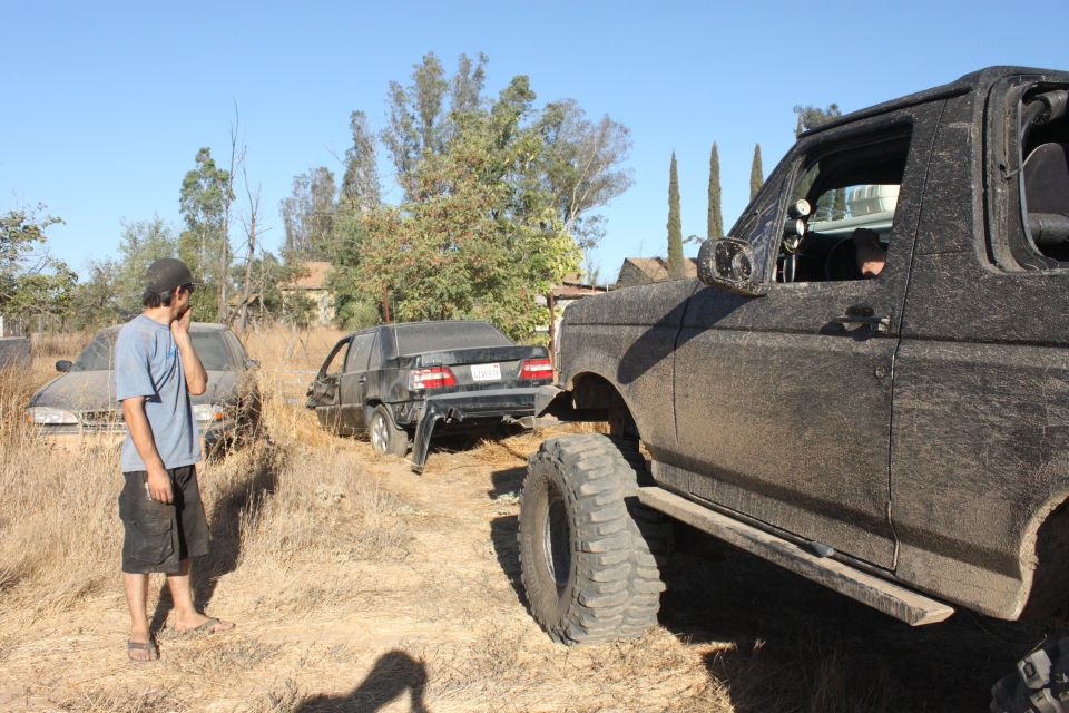 Mud-covered 1992 Ford Bronco, 3/4 front view, with a damaged black car behind it