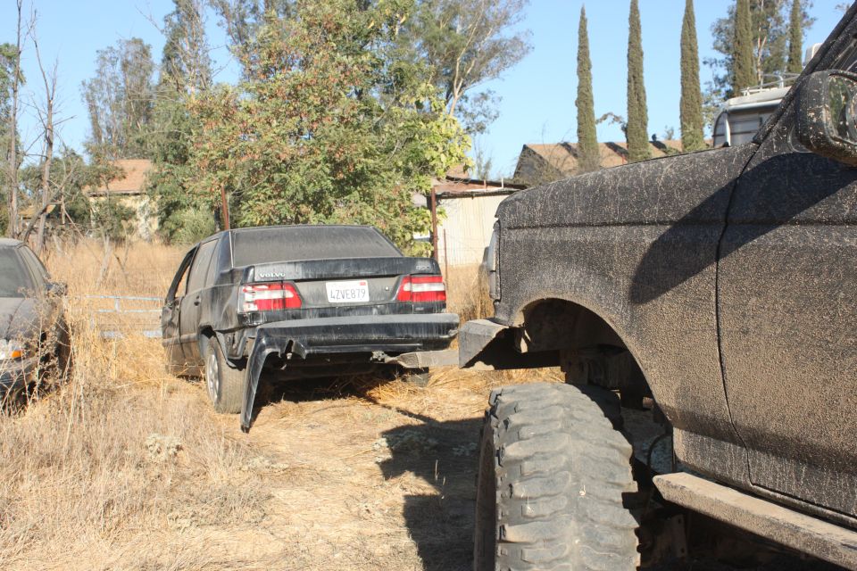 Mud-covered truck's fender and tire in foreground, damaged sedan in background