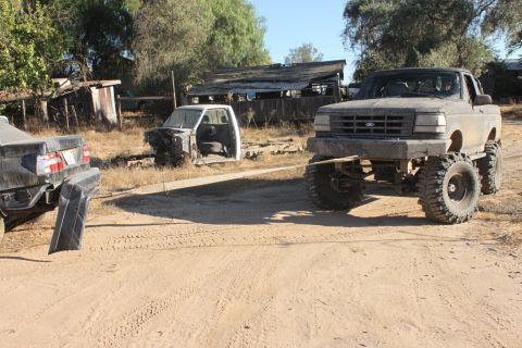 Lifted Ford pickup truck in front of a car chassis and another vehicle's rear end