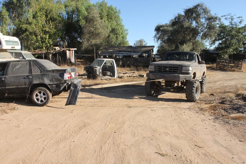 Gray 1992 Ford Bronco with large tires towing a black sedan