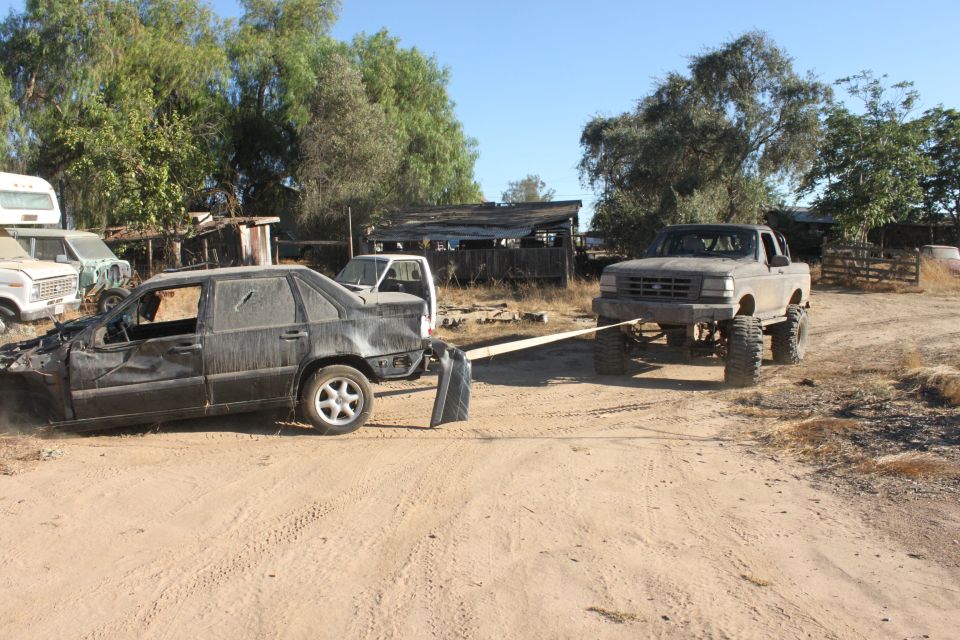 Damaged black sedan towed by a lifted gray pickup truck in a junkyard
