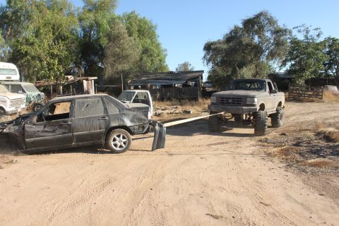 Gray pickup truck towing a wrecked black sedan on a dirt road