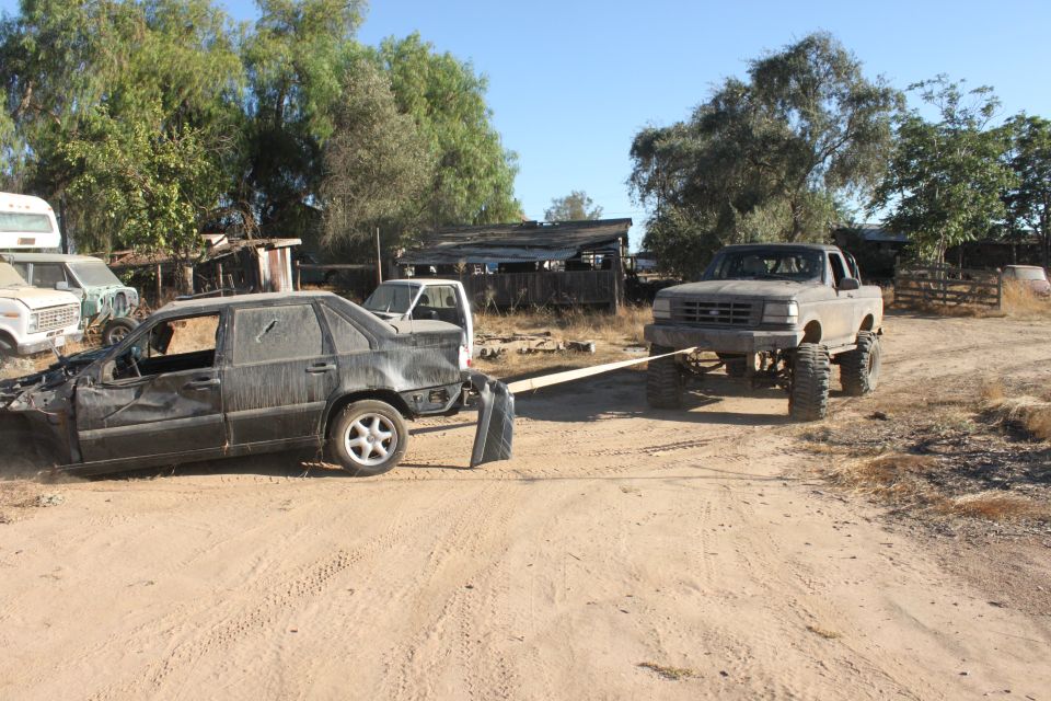 Gray pickup truck towing a wrecked black sedan on a dirt road