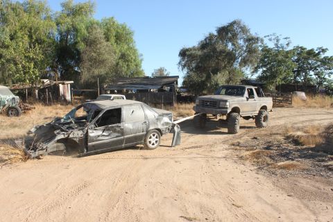 Lifted pickup truck towing a heavily damaged sedan on a dirt road
