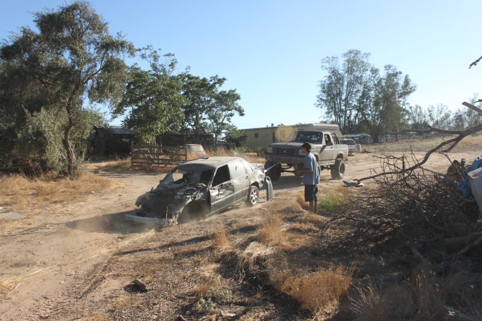 Wrecked car being towed by a lifted pickup truck on a dirt road