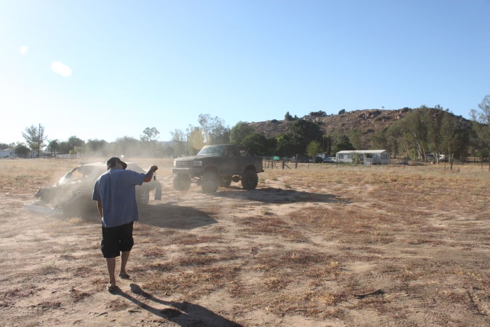 Black 1992 Ford Bronco lifted and driving in a dusty field with a person watching