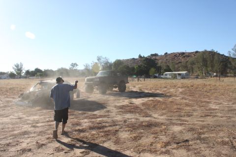 Two trucks in a dusty field with a person walking