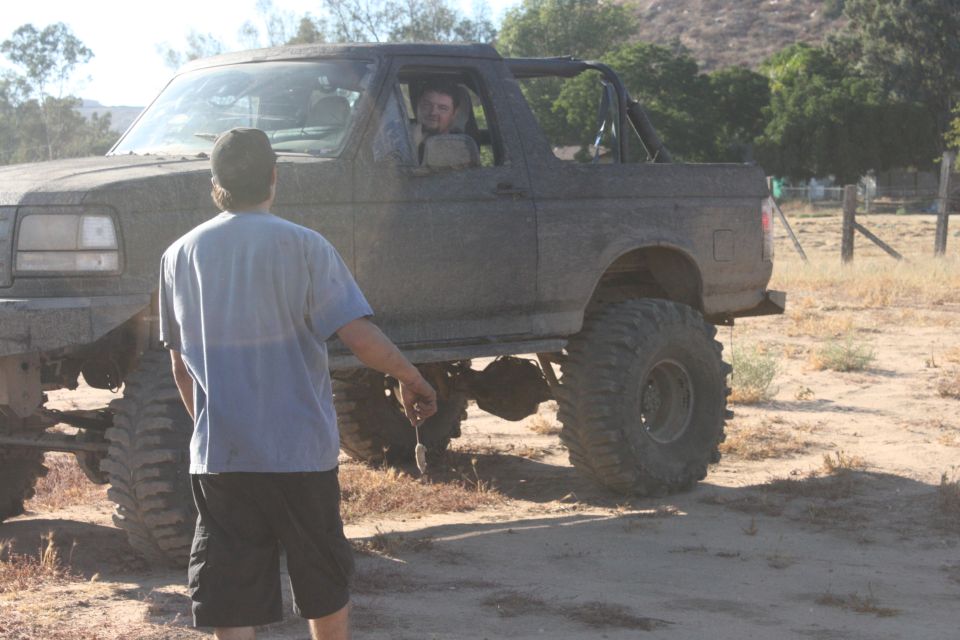 Muddy 1992 Ford Bronco with large tires, lifted suspension, and a roll cage visible. Driver is in the cab