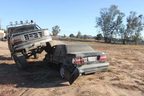Black Ford F-Series truck crushing a dark sedan in a dirt lot