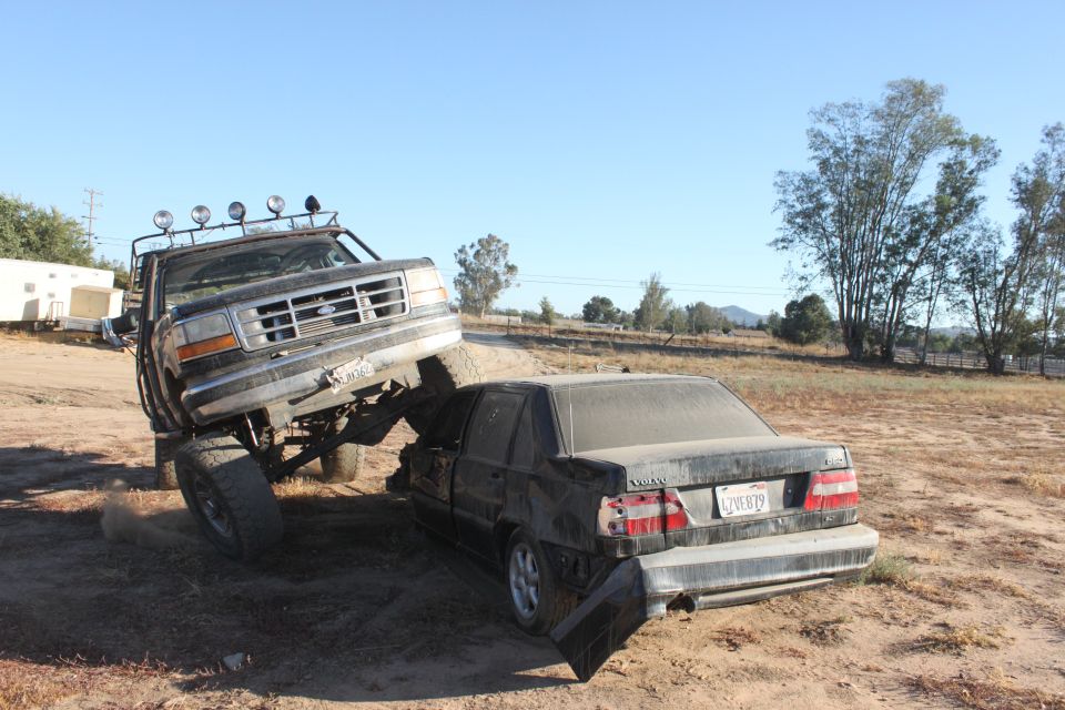 1992 Ford Bronco crushing a black Volvo sedan in a dirt lot