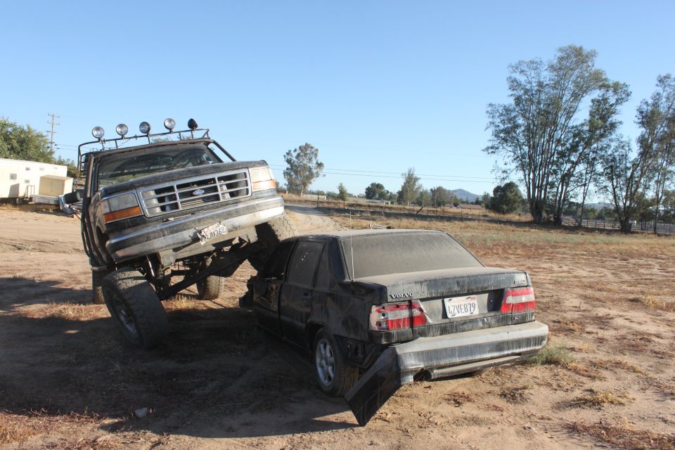 1992 Ford F-Series truck on a wrecked Volvo sedan in a dirt lot
