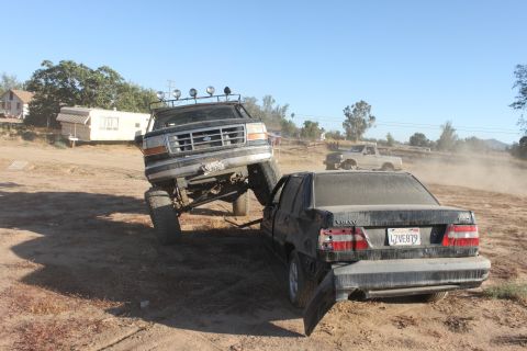 Black 1992 Ford Bronco lifted high, front end crushing a black Volvo sedan