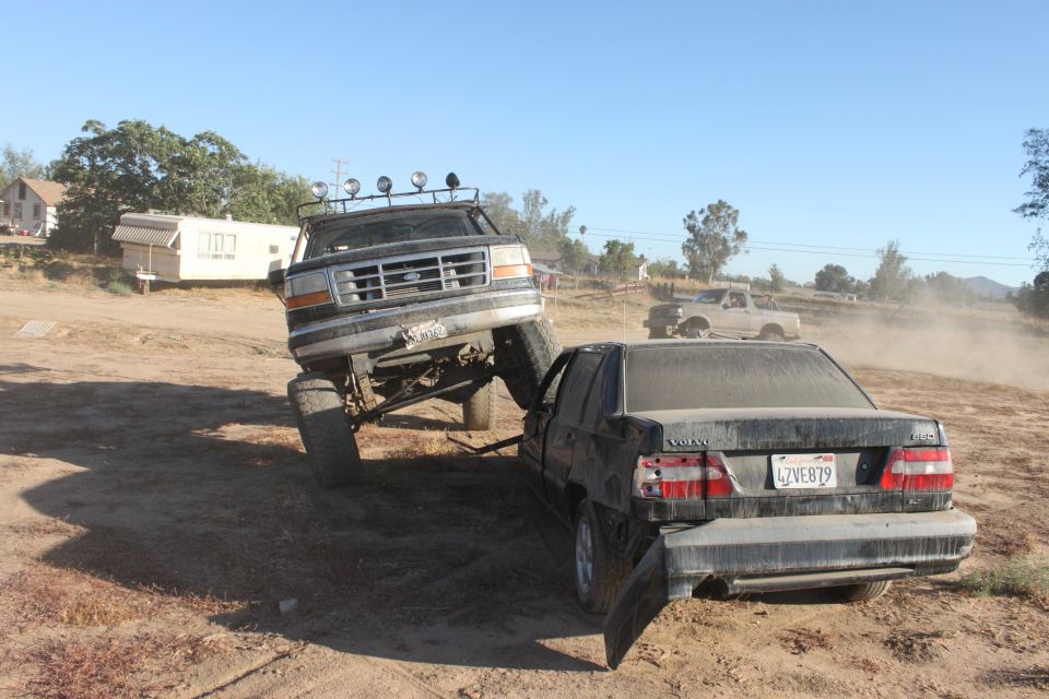 Black 1992 Ford Bronco lifted high, front end crushing a black Volvo sedan