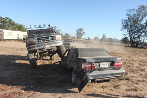 Lifted 1992 Ford Bronco on a sedan in a dusty outdoor scene