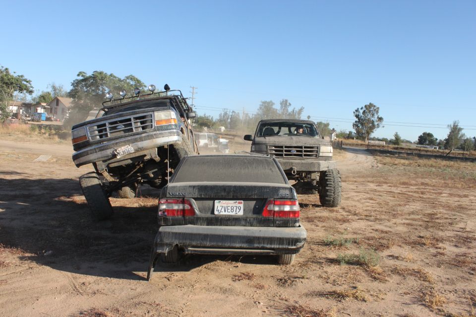 Lifted 1992 Ford F-150 on left, another lifted Ford truck behind it, and a Volvo sedan in front. Dirt lot scene