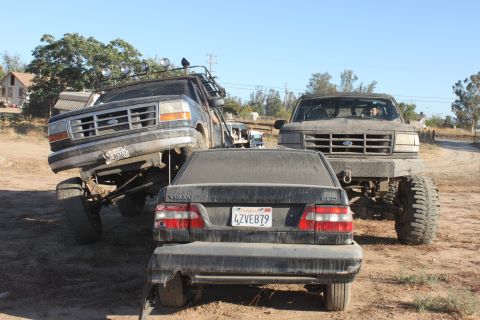1992 Ford Bronco lifted high, another lifted Ford truck, and a Volvo sedan parked together