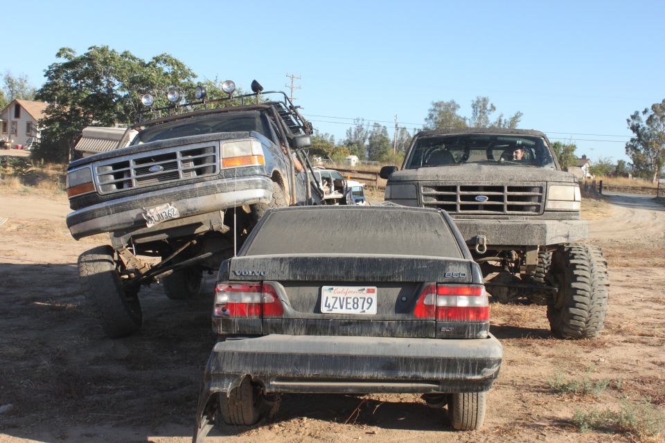 1992 Ford Bronco lifted high, another lifted Ford truck, and a Volvo sedan parked together