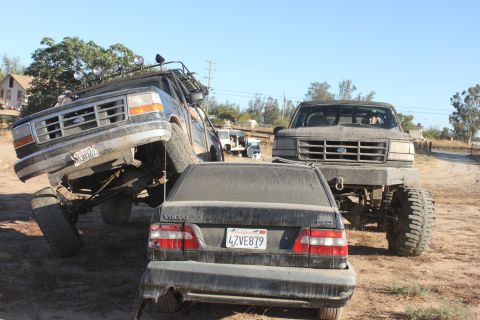 1992 Ford Bronco lifted with off-road lights, front grille visible, next to another lifted Ford truck and a bl