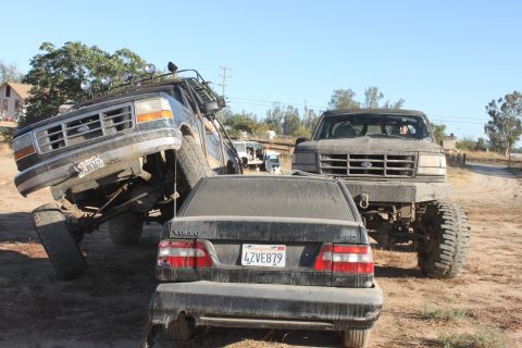 1992 Ford Bronco tilted on its side, front grille visible. Volvo sedan and another Ford truck nearby