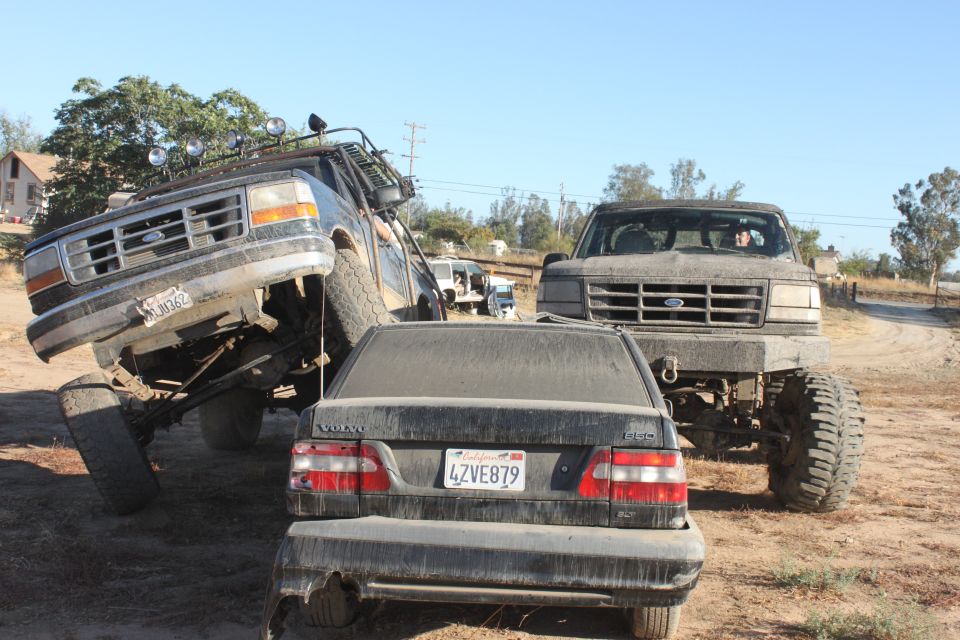 1992 Ford Bronco tilted on its side, front grille visible. Volvo sedan and another Ford truck nearby