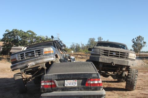 Two lifted 1992 Ford Broncos and a Volvo sedan on a dirt lot