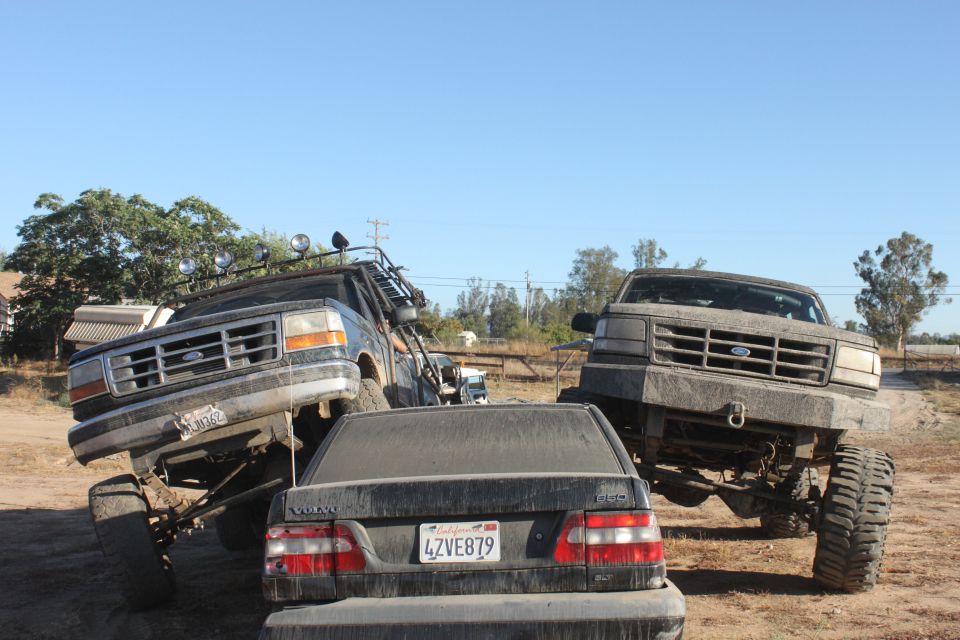 Two lifted 1992 Ford Broncos and a Volvo sedan on a dirt lot