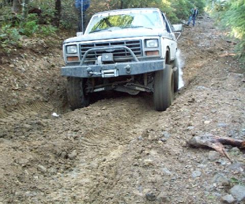 1982 Ford Bronco - This 1980s Ford Bronco is navigating a challenging muddy trail, showing its front end as it climbs.