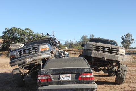 1992 Ford Bronco lifted and tilted, front grille visible, with a Volvo sedan in the foreground