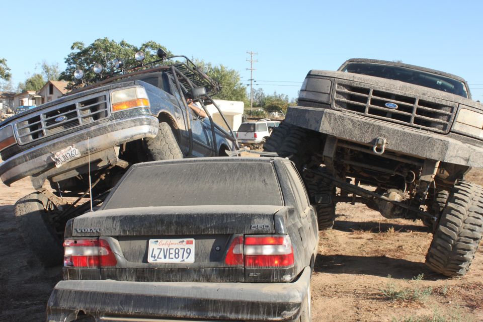 1992 Ford Bronco lifted high, another lifted Ford truck, and a Volvo sedan on dirt