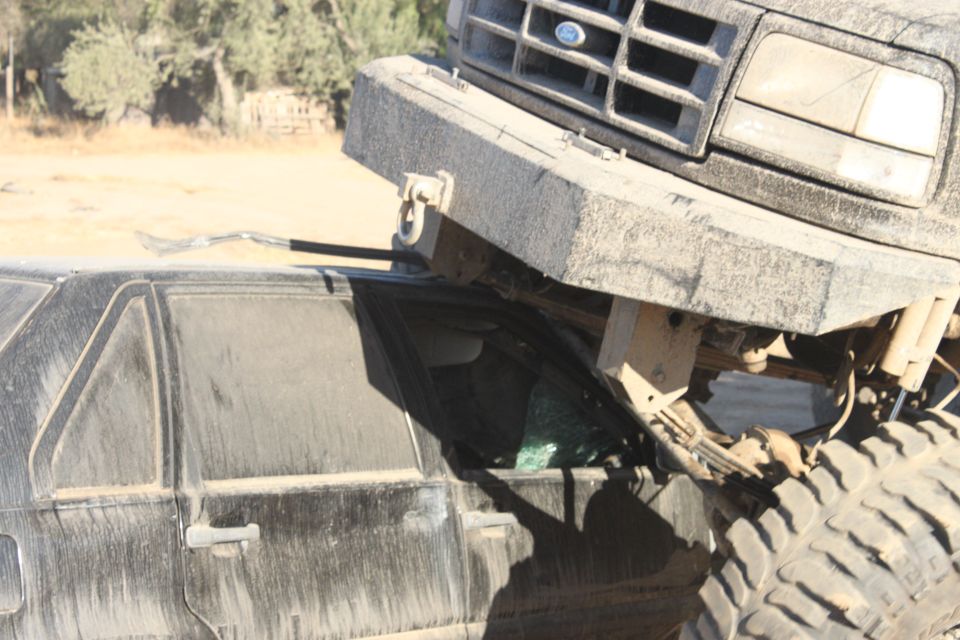 Monster truck on top of a crushed car