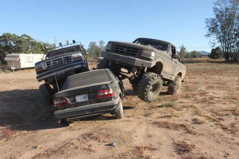 1992 Ford Bronco lifted over a sedan, with another lifted truck nearby
