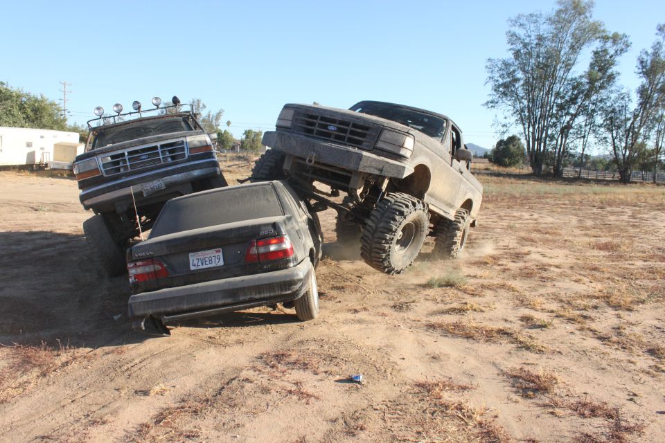 Lifted 1992-1996 Ford F-150 truck on top of a Volvo sedan, another Ford truck behind