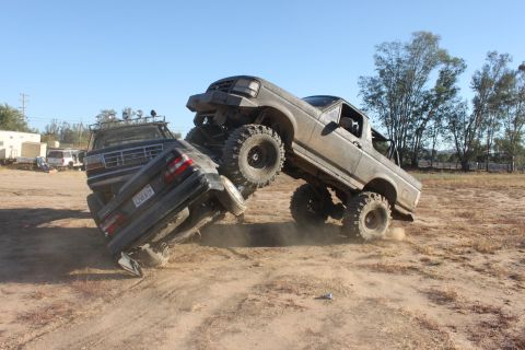 Gray 1992 Ford Bronco on top of a crushed car, with another truck behind