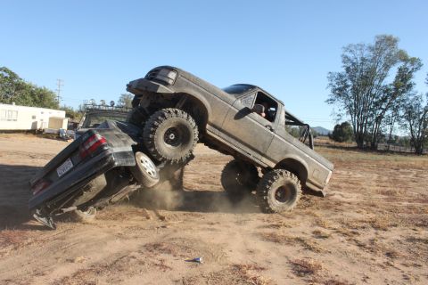 Muddy off-road truck on top of a car, tires kicking up dirt